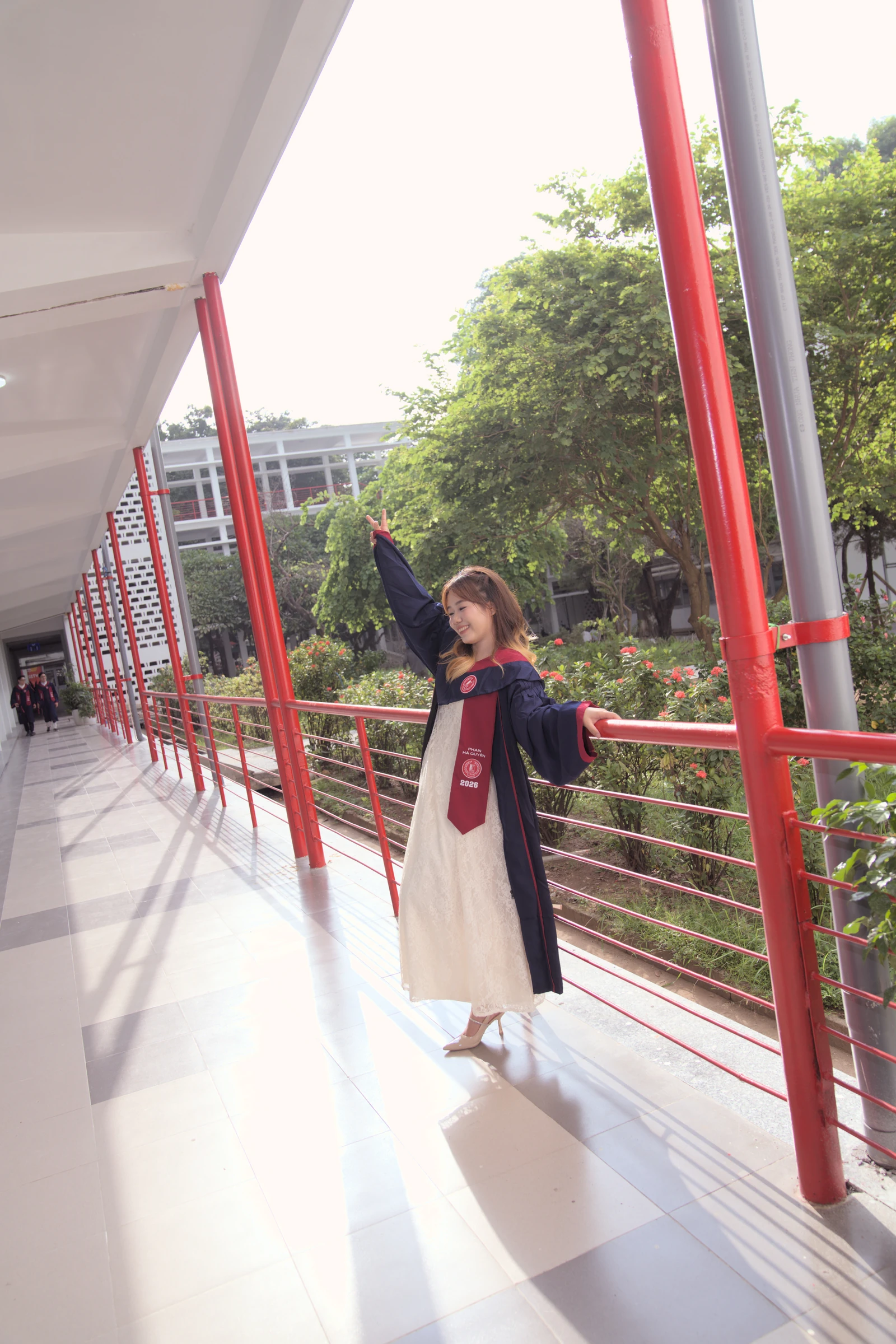 Quyên on a bright balcony with red railings and green trees