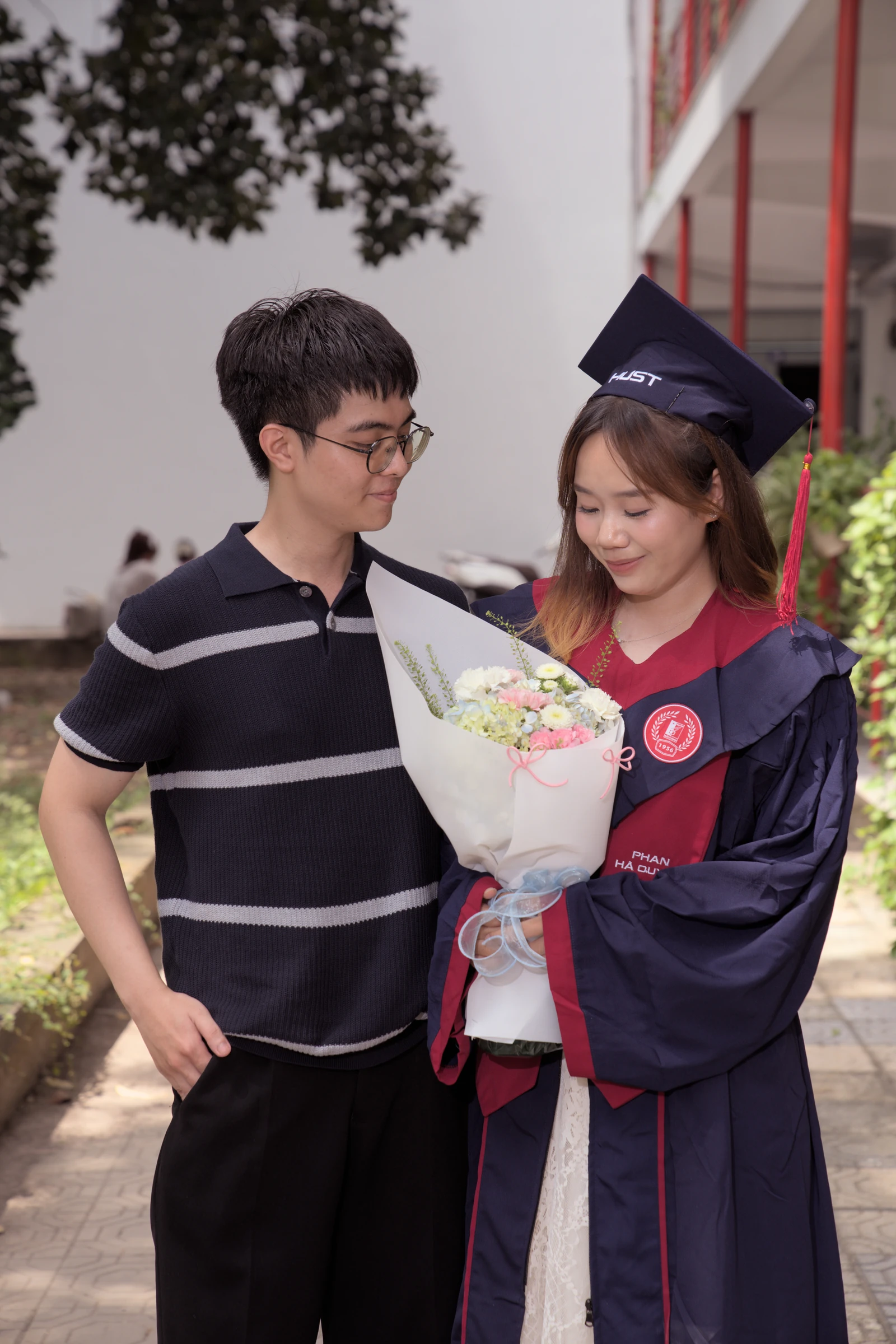 Quyên holding a bouquet beside a companion on graduation day