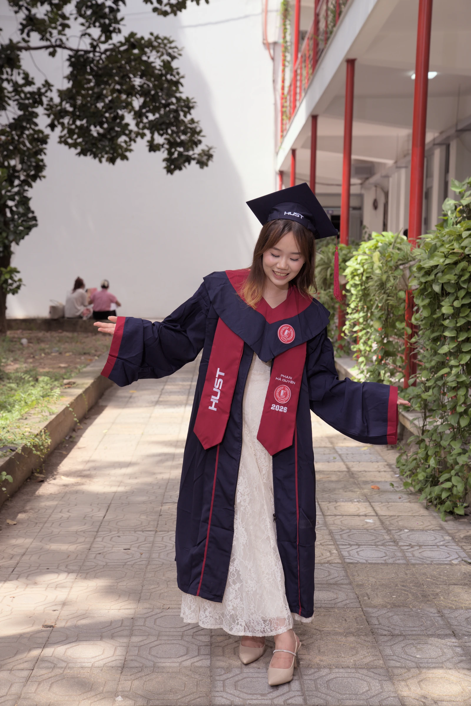 Quyên smiling and spreading the sleeves of her graduation gown